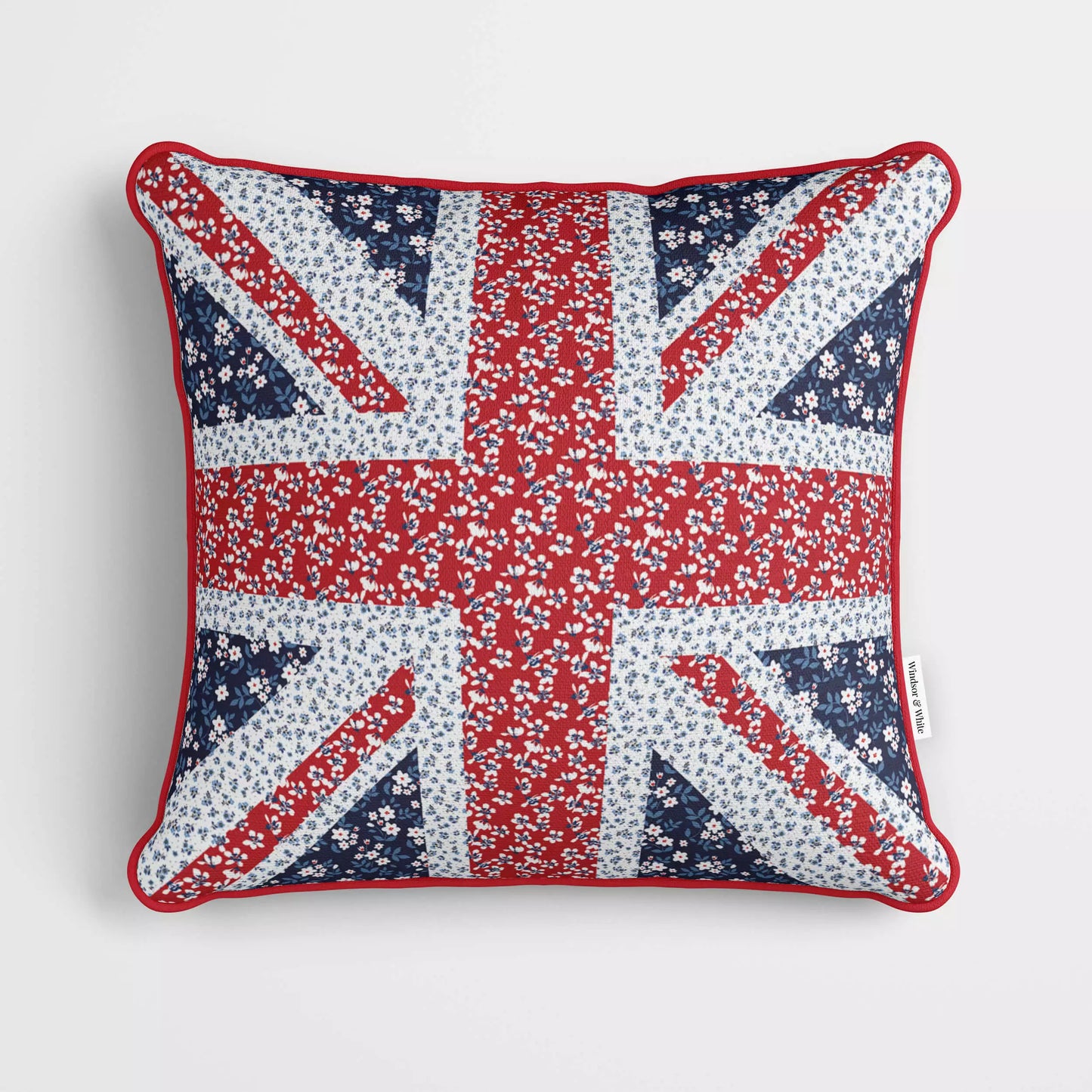 A cushion featuring the Union Jack on a velvet floral fabric, with red piping around the edge.