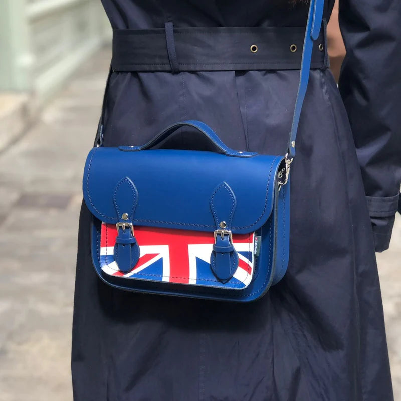 A woman wearing a midi satchel bag, in blue, featuring the Union Jack on the front pocket