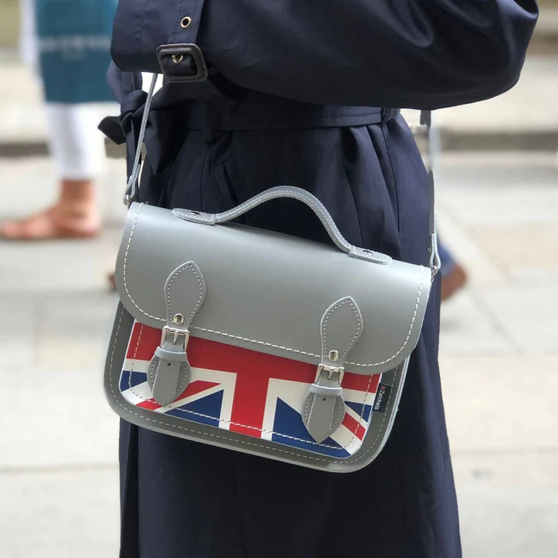 A woman wearing a midi satchel bag, in grey, featuring the Union Jack on the front pocket