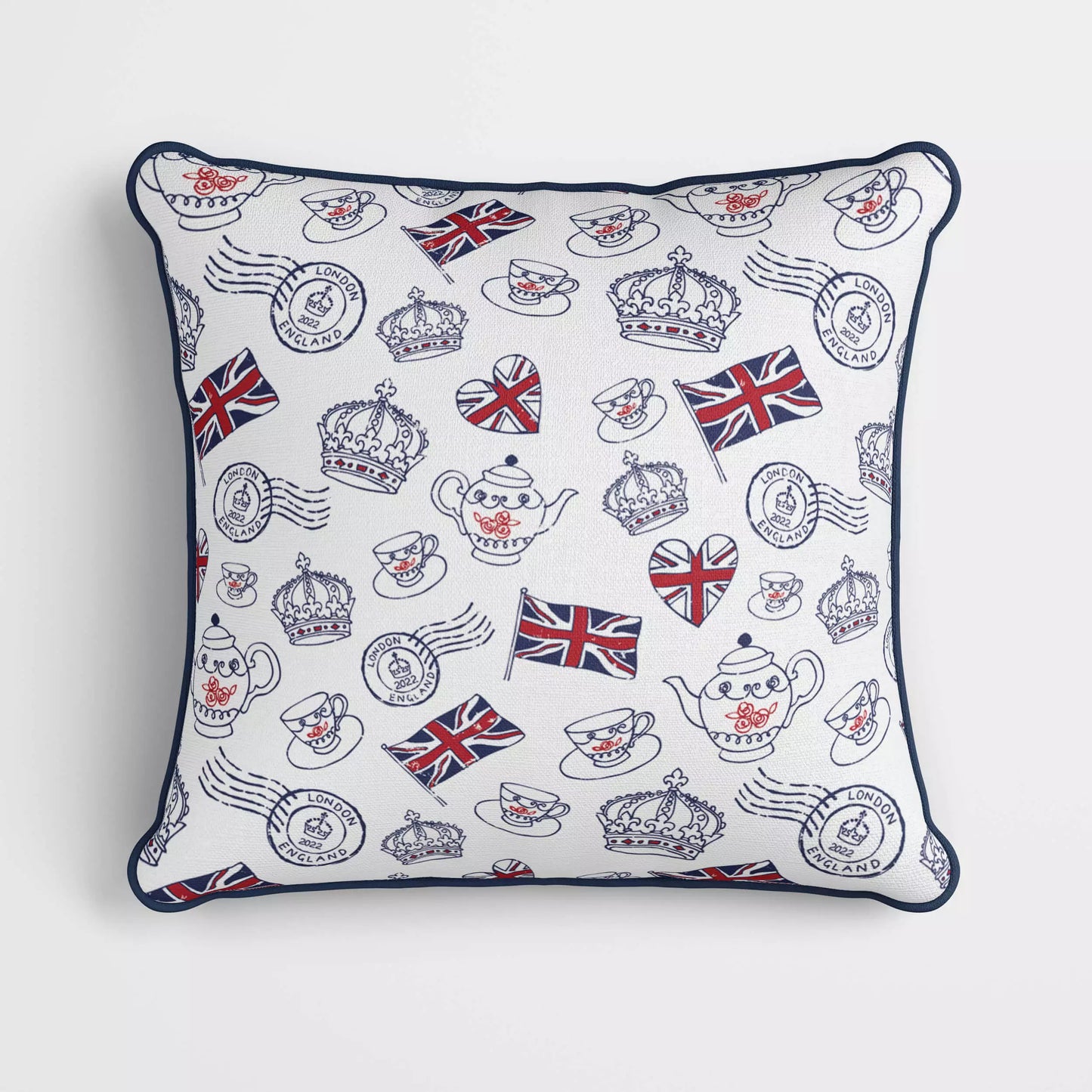 A velvet cushion with figures of the Union Jack, crowns, teacups and saucers, teapots and London stamps printed on it, with blue piping around the edge.